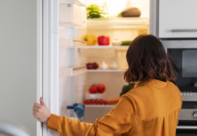 Une femme ouvre son frigo pour y prendre de la nourriture